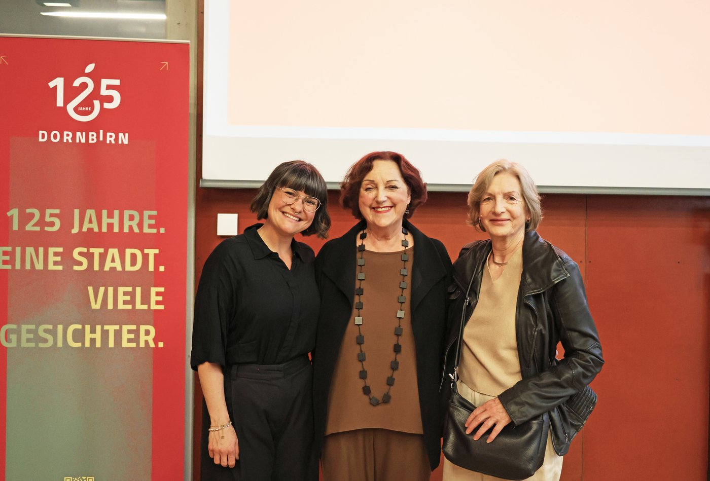 Marilena Tumler, Roswitha Fessler und Lisa Althaus bei der Er&ouml;ffnung des digitalen Frauenspuren-Rundgangs im Stadtarchiv Dornbirn vor einem 125-Jahre-Dornbirn-Banner.